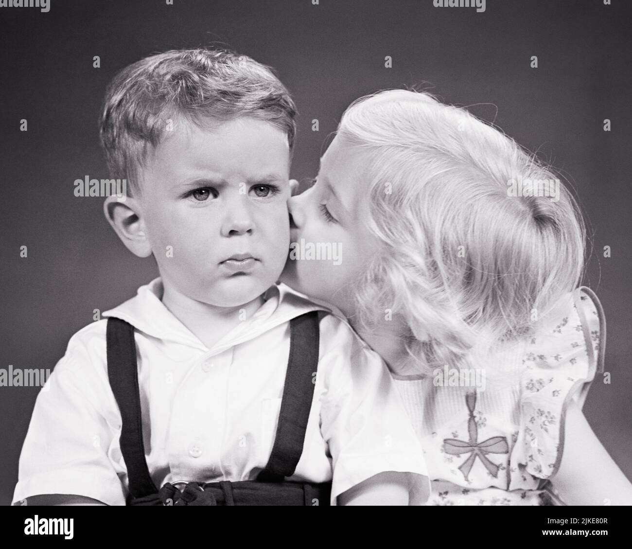 1940s LITTLE BLONDE GIRL KISSING HER SAD GRUMPY BABY BROTHER ON THE CHEEK - j3827 HAR001 HARS WORRY STRONG FAMILIES LIFESTYLE FEMALES BROTHERS STUDIO SHOT MOODY HOME LIFE COPY SPACE FRIENDSHIP HALF-LENGTH PERSONS CARING MALES SIBLINGS SISTERS TROUBLED B&W CONCERNED SADNESS MOOD SIBLING CONNECTION CONCEPTUAL GLUM FRIENDLY BABY BOY PERSONAL ATTACHMENT AFFECTION EMOTION GROWTH MISERABLE PECK SMOOCH TOGETHERNESS BLACK AND WHITE CAUCASIAN ETHNICITY HAR001 OLD FASHIONED Stock Photo