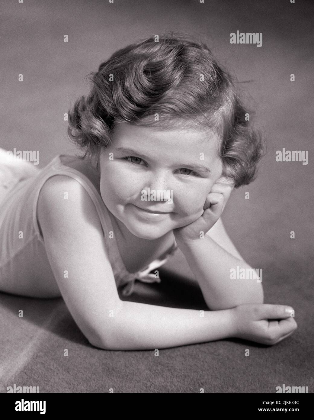 1930s CUTE LITTLE GIRL LYING ON HER STOMACH RESTING HER HEAD IN HER HAND SMILING LOOKING UP AT CAMERA - j5122 HAR001 HARS B&W RESTING EYE CONTACT BRUNETTE PRETTY HAPPINESS CHEERFUL HIGH ANGLE STOMACH PRIDE SMILES JOYFUL STYLISH PLEASANT AGREEABLE CHARMING GROWTH JUVENILES LOOKING UP LOVABLE PLEASING RELAXATION ADORABLE APPEALING BLACK AND WHITE CAUCASIAN ETHNICITY HAR001 OLD FASHIONED Stock Photo