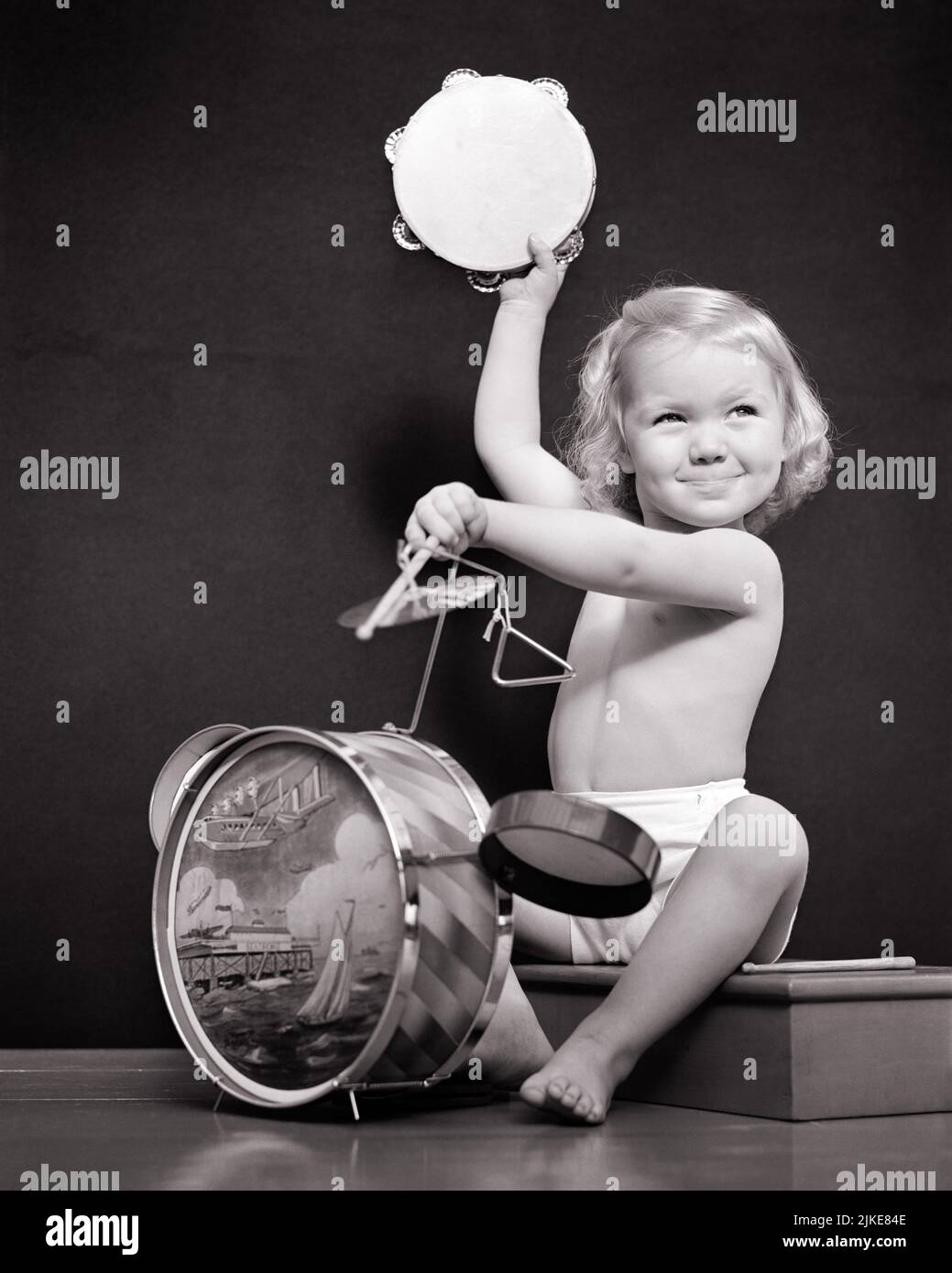 1940s SMILING BLONDE GIRL PLAYING DRUMS SET WITH CYMBALS AND TRIANGLE RAISING A TAMBOURINE LIKE A ONE MAN BAND LOOKING UP - j4802 HAR001 HARS HEALTHINESS HOME LIFE COPY SPACE HALF-LENGTH DRUMS TRIANGLE INSPIRATION PERFORMANCE RAISING ENTERTAINMENT B&W GOALS CYMBALS HAPPINESS CHEERFUL DISCOVERY PERFORMER AND EXCITEMENT LOW ANGLE PRIDE UP ENTERTAINER LIKE OCCUPATIONS SMILES MUSICAL INSTRUMENT BARE FEET ACTORS DRUMMER JOYFUL ONE-MAN BAND DRUMMING ENTERTAINERS GROWTH JUVENILES ONE MAN BAND PERFORMERS SOLUTIONS TAMBOURINE BLACK AND WHITE CAUCASIAN ETHNICITY HAR001 OLD FASHIONED Stock Photo