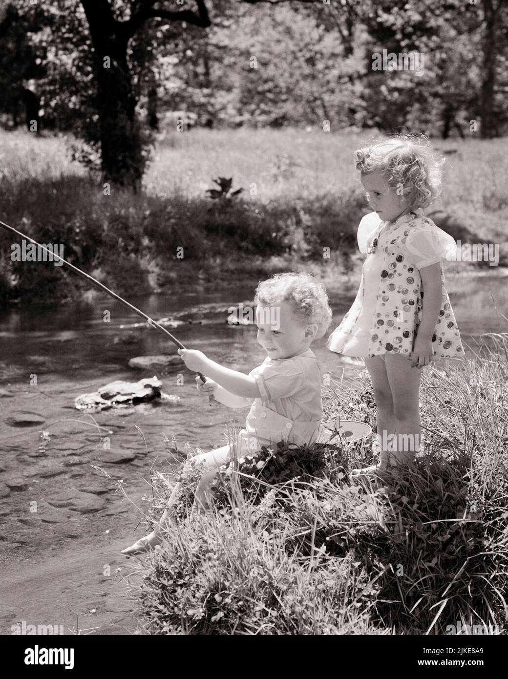 1940s LITTLE BLONDE BOY AND GIRL ON BANK OF STREAM BOY WITH STICK FISHING IN THE WATER GIRL STANDING BEHIND HIM - j6081 HAR001 HARS SAFETY JOY LIFESTYLE FEMALES WINNING BROTHERS RURAL HEALTHINESS NATURE COPY SPACE FRIENDSHIP FULL-LENGTH PERSONS STREAM MALES SIBLINGS SISTERS B&W SUMMERTIME HAPPINESS HIGH ANGLE ADVENTURE LEISURE AND RECREATION SIBLING FRIENDLY STYLISH ANGLING BABY BOY PLEASANT AGREEABLE CHARMING COOPERATION GROWTH HIM IDYLLIC LOVABLE PLEASING SEASON TOGETHERNESS ADORABLE APPEALING BLACK AND WHITE CAUCASIAN ETHNICITY HAR001 OLD FASHIONED Stock Photo