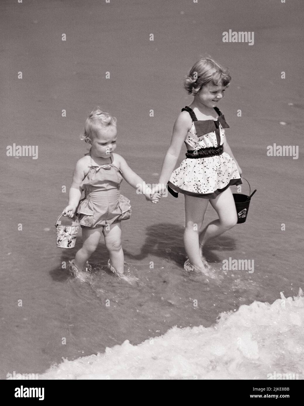 1950s-two-girls-holding-hands-and-sand-pails-wearing-bathing-suits-walking-in-surf-holding-hands-big-and-little-sisters-j699-har001-hars-lifestyle-ocean-females-healthiness-copy-space-friendship-full-length-caring-siblings-surf-sisters-bw-summertime-shore-happiness-high-angle-adventure-leisure-protection-and-excitement-recreation-pails-holding-hands-beaches-holidays-sibling-connection-little-sister-friendly-sandy-stylish-baby-sister-salt-water-growth-juveniles-older-sister-season-togetherness-vacations-baby-girl-big-sister-black-and-white-caucasian-ethnicity-har001-old-fashioned-2JKE8BB.jpg