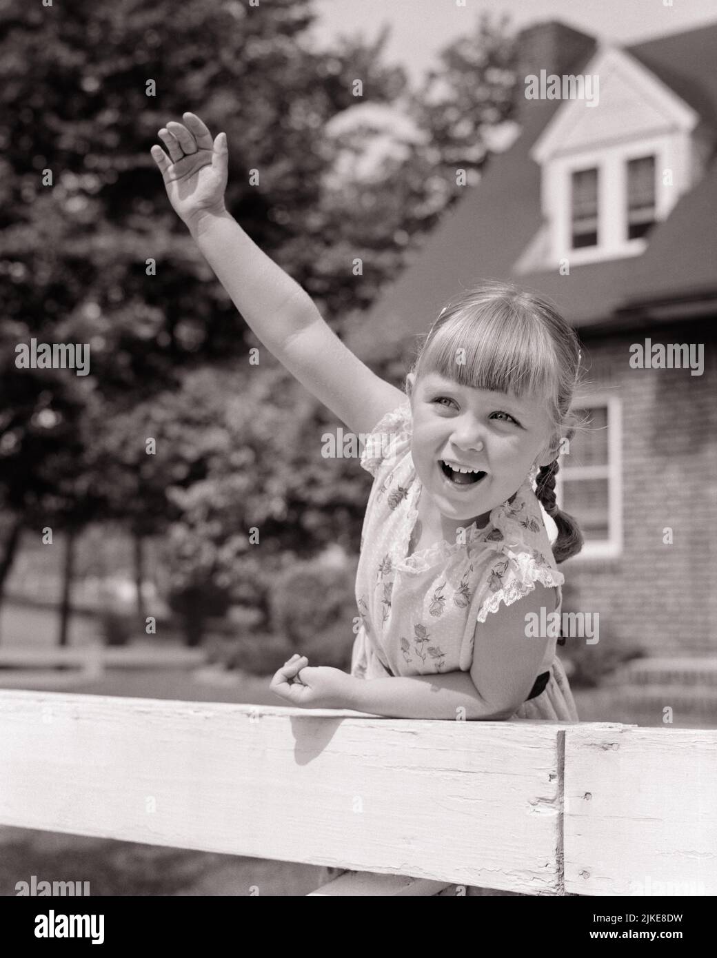 1950s 1960s EXCITED SMILING LITTLE GIRL WITH BANGS LEANING ON FENCE AND WAVING WITH RAISED ARM - j7590 HAR001 HARS LIFESTYLE SATISFACTION FEMALES HOUSES RURAL HEALTHINESS HOME LIFE COPY SPACE FRIENDSHIP HALF-LENGTH INSPIRATION RESIDENTIAL BUILDINGS GESTURING B&W SUMMERTIME EYE CONTACT HAPPINESS CHEERFUL HELLO AND EXCITEMENT EXTERIOR LOW ANGLE GESTURES HOMES SMILES CONCEPTUAL JOYFUL RESIDENCE GROWTH JUVENILES SEASON BANGS BLACK AND WHITE CAUCASIAN ETHNICITY HAR001 OLD FASHIONED Stock Photo
