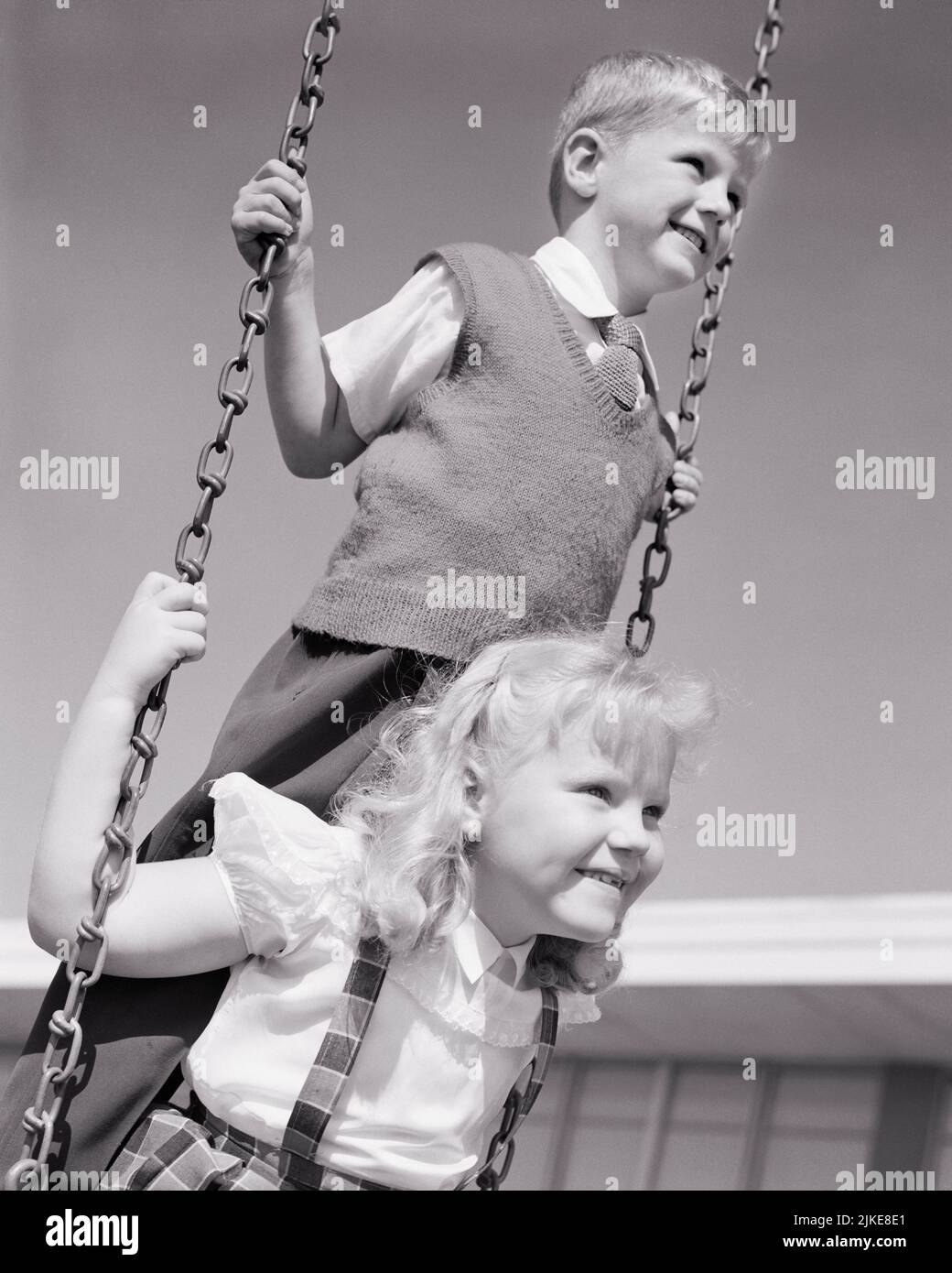 1950s BLONDE BOY AND GIRL ON PLAYGROUND SWING SET GIRL SITTING ON SWING SEAT AND BOY STANDING BEHIND HER - j7551 HAR001 HARS 1 SEAT JUVENILE ELEMENTARY BLOND FRIEND BALANCE TEAMWORK PLEASED JOY LIFESTYLE FEMALES BROTHERS HEALTHINESS COPY SPACE FRIENDSHIP HALF-LENGTH PERSONS MALES SIBLINGS SISTERS B&W SCHOOLS GRADE HAPPINESS CHEERFUL AND EXCITEMENT RECESS RECREATION PRIMARY SIBLING SMILES CONNECTION FRIENDLY JOYFUL GRADE SCHOOL TOGETHERNESS BLACK AND WHITE CAUCASIAN ETHNICITY HAR001 OLD FASHIONED Stock Photo