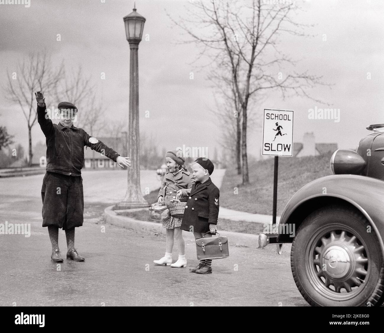 1930s TEEN BOY CROSSING GUARD STOPPING TRAFFIC YOUNG BOY GIRL CARRYING LUNCH PAILS BOOK BAG CROSSING STREET BY SLOW SCHOOL SIGN - j8157 HAR001 HARS BUSY NOSTALGIA BROTHER GUARD CROSSING OLD FASHION AUTO SISTER 1 JUVENILE ELEMENTARY STYLE VEHICLE SAFETY TEAMWORK LIFESTYLE SATISFACTION FEMALES BROTHERS HOME LIFE NATURE COPY SPACE FULL-LENGTH AUTOMOBILE CARING MALES RISK TEENAGE BOY SIBLINGS SISTERS TRANSPORTATION B&W SCHOOLS GRADE PROTECTION AUTOS LEADERSHIP FALL SEASON PAILS PRIDE PRIMARY SIBLING CONNECTION PATROL CONCEPTUAL AUTOMOBILES STOPPING VEHICLES CROSSING GUARD COOPERATION GRADE SCHOOL Stock Photo