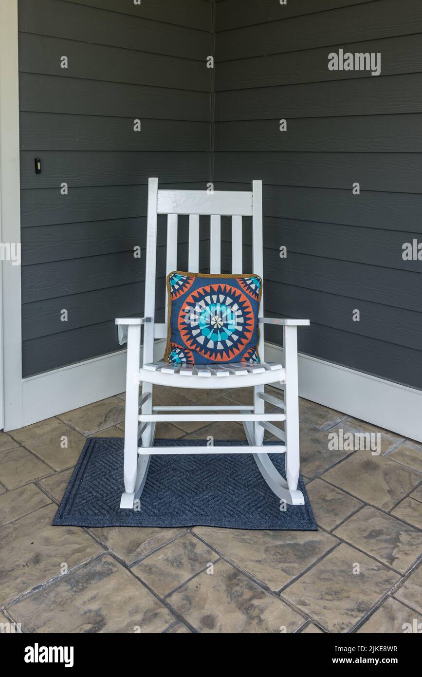 A stamped concrete front porch with a white rocking chair with a colorful pillow Stock Photo