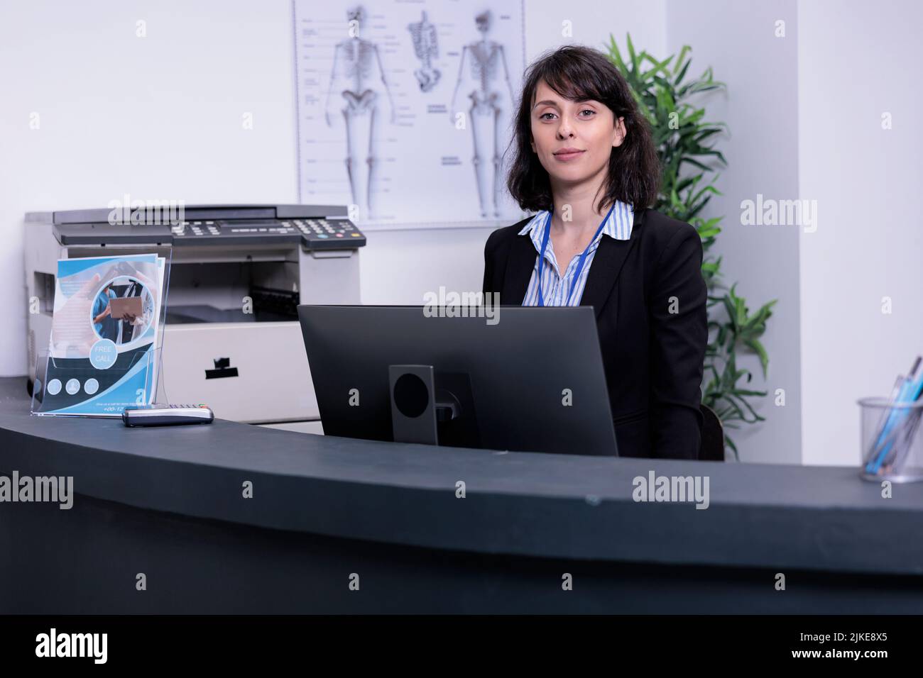 Portrait of smiling hospital receptionist standing at front desk waiting for appointments in private hospital. Professional healthcare worker greeting patients in private practice clinic lobby. Stock Photo