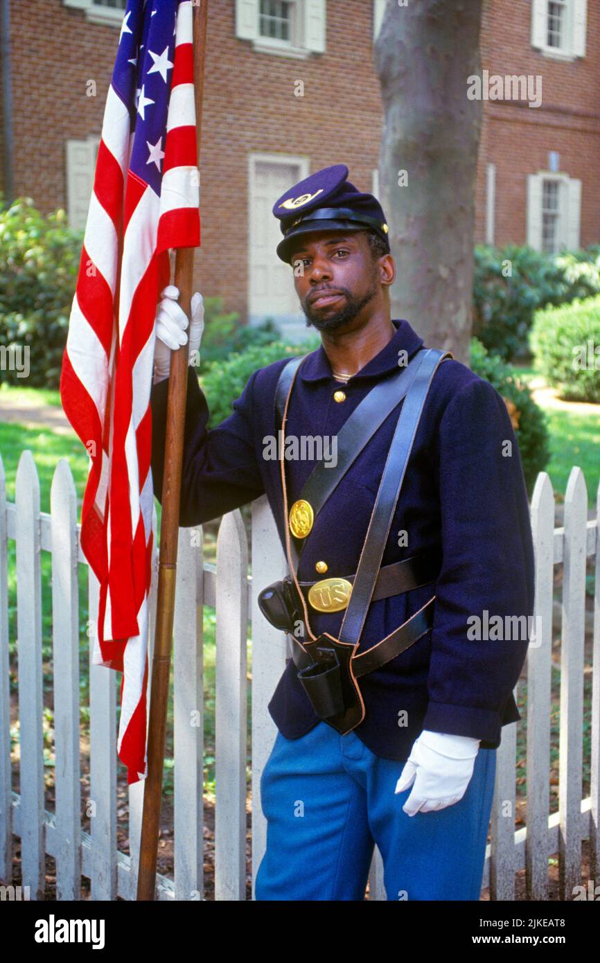 1990s AFRICAN AMERICAN MAN UNION SOLDIER UNIFORM CIVIL WAR REENACTOR LOOKING AT CAMERA HOLDING AMERICAN FLAG PHILADELPHIA PA USA - kp6430 NET002 HARS HALF-LENGTH PERSONS MALES EYE CONTACT FREEDOM WARS ADVENTURE UNION AFRICAN-AMERICANS AFRICAN-AMERICAN EXTERIOR PA BLACK ETHNICITY FACIAL HAIR UNIFORMS REMINDER CONCEPTUAL 1860s BLACKS STARS AND STRIPES REENACTOR UNIFORMED CONTRIBUTION OLD GLORY BEARDS RED WHITE AND BLUE YOUNG ADULT MAN AMERICAN CIVIL WAR AMERICAN FLAG BATTLES CIVIL WAR CONFLICTS OLD FASHIONED AFRICAN AMERICANS Stock Photo