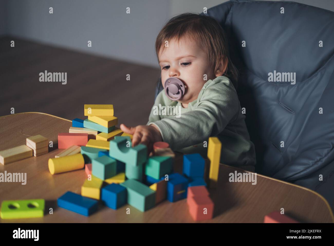 Baby girl in sucking pacifier playing with construction toy blocks ...