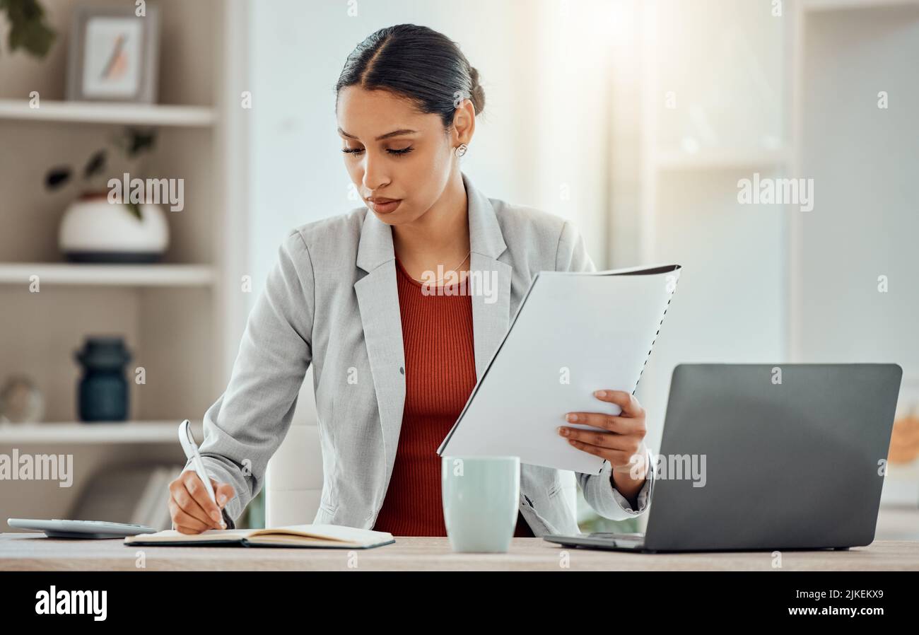 African Business woman planning, taking notes and writing in a notebook while reading a report, document or paperwork in an office alone at work. One Stock Photo