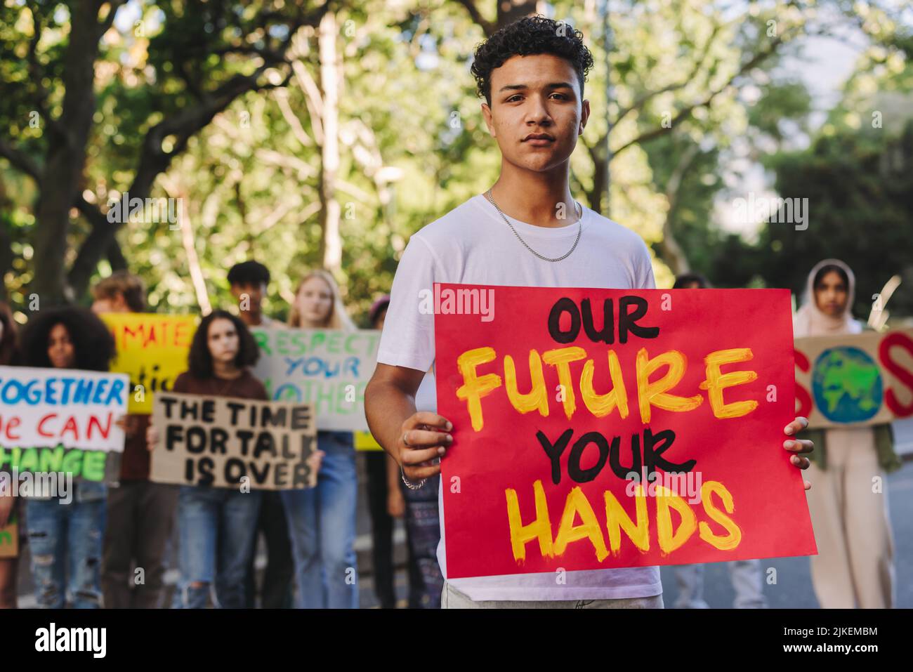 Teenage boy looking at the camera while leading a march against climate change. Group of multicultural youth activists protesting against global warmi Stock Photo