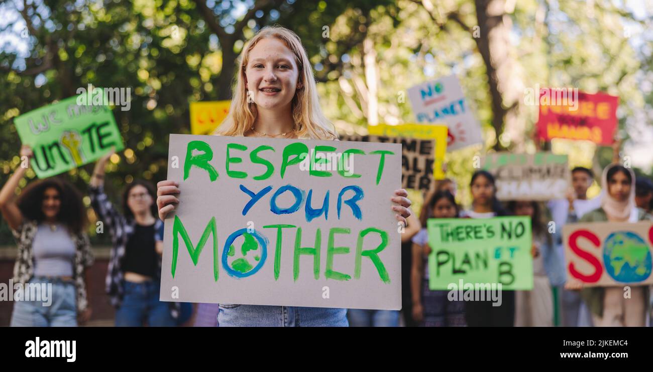 Happy youth activist smiling at the camera while leading a march against climate change. Group of multiethnic teenagers protesting against global warm Stock Photo