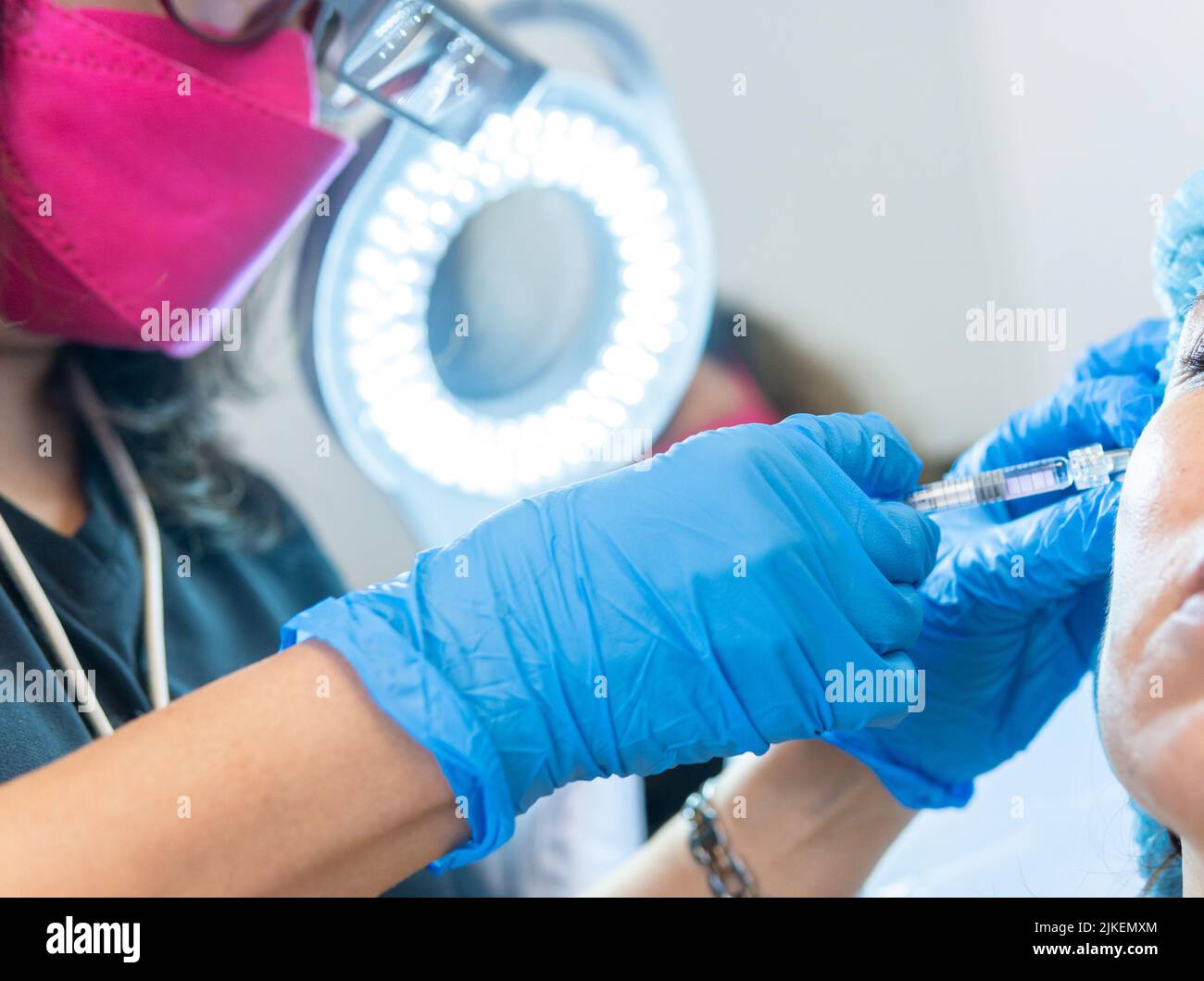 Close-up of a female doctor applying hyaluronic acid with a syringe to a patient illuminated by a dermatology led lamp Stock Photo