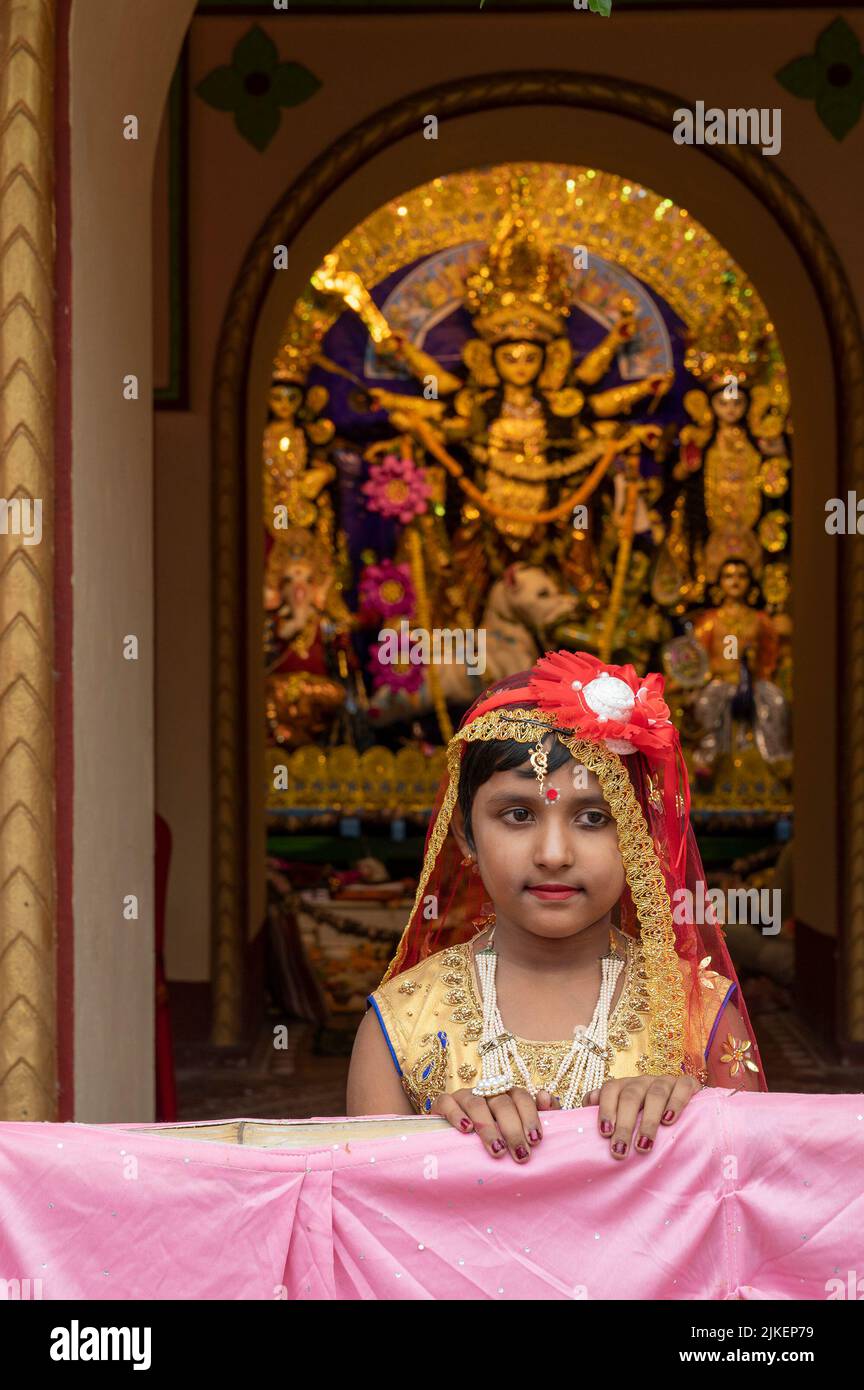 Howrah,India -October 26th,2020 : Bengali girl child in festive dress, smiling and posing with Goddess Durga in background, inside decorated home. Stock Photo