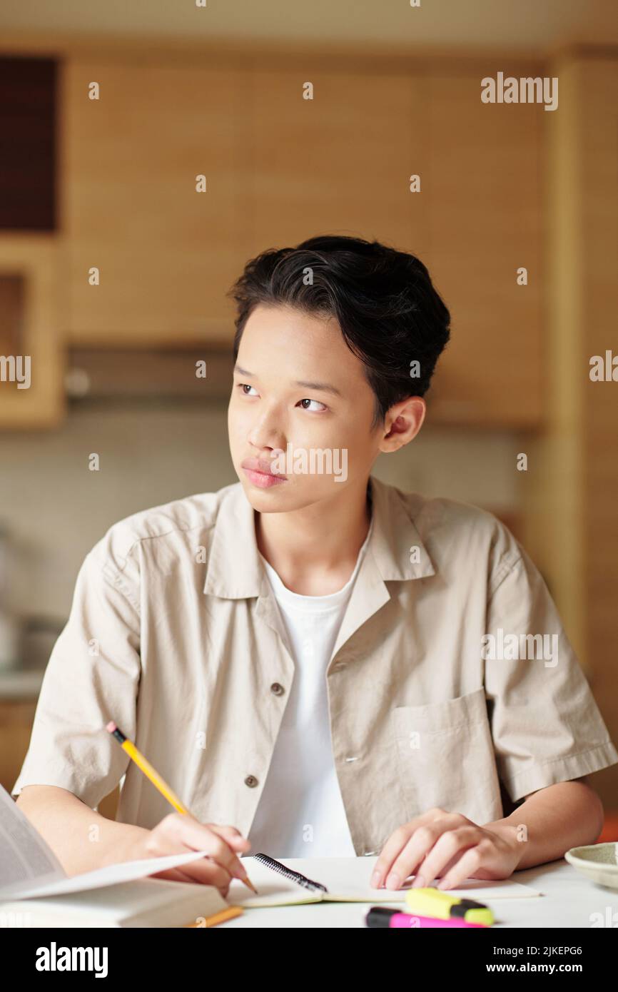 Portrait of pensive teenage boy looking outside through kitchen window ...