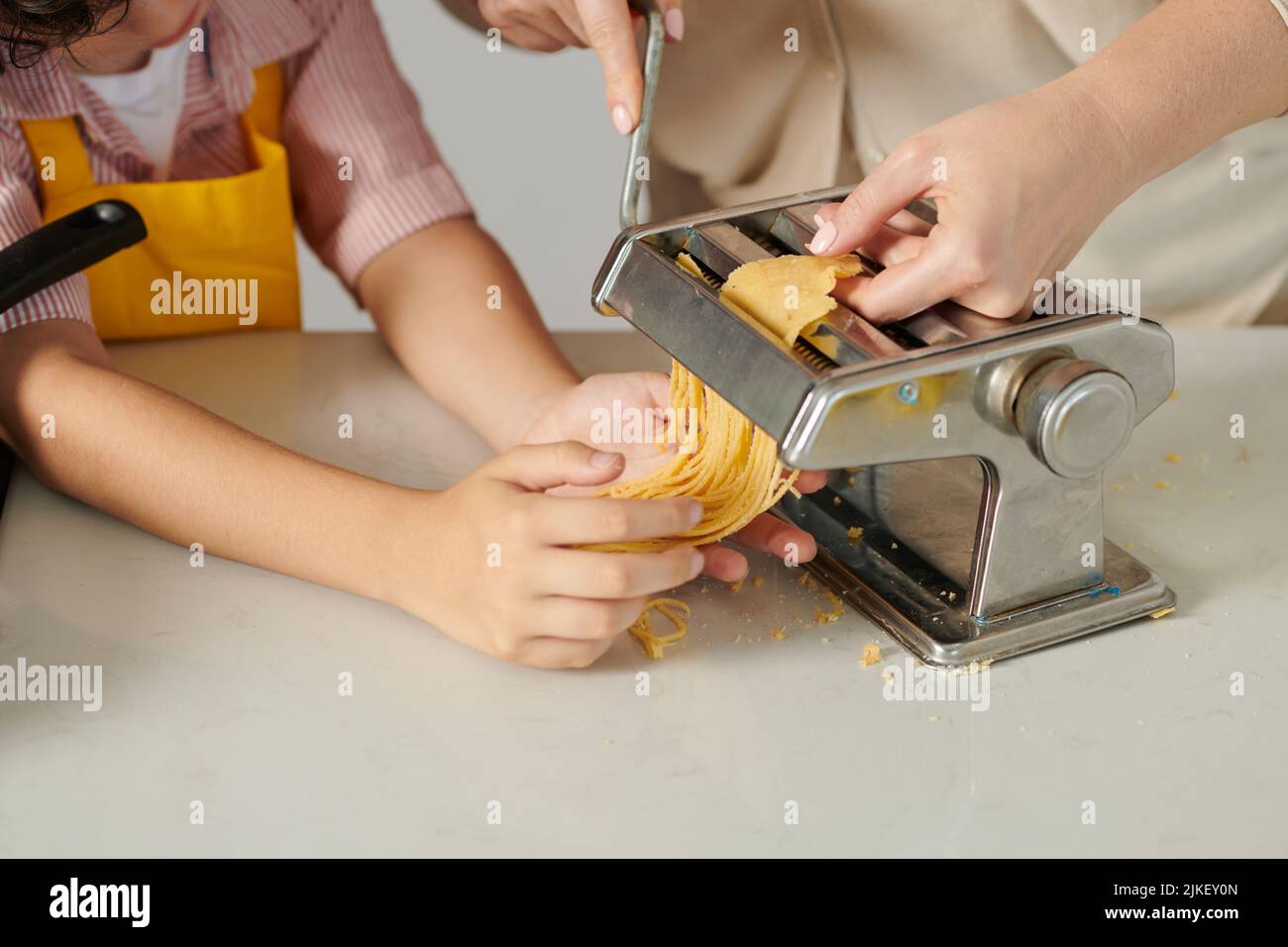 Curious preteen boy helping mother with making spaghetti with pasta
