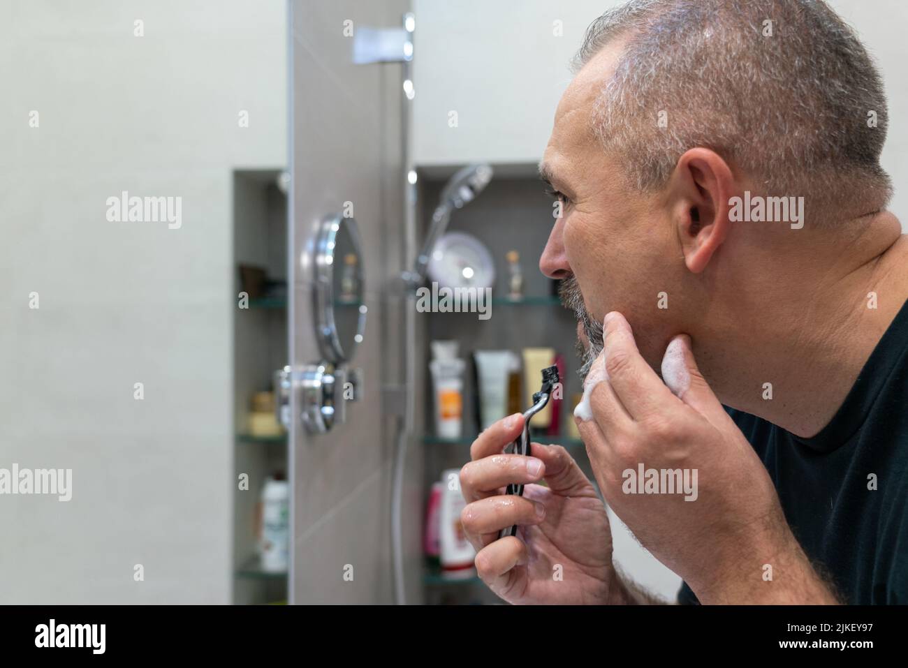 Middle-aged handsome man using razor in bathroom Stock Photo