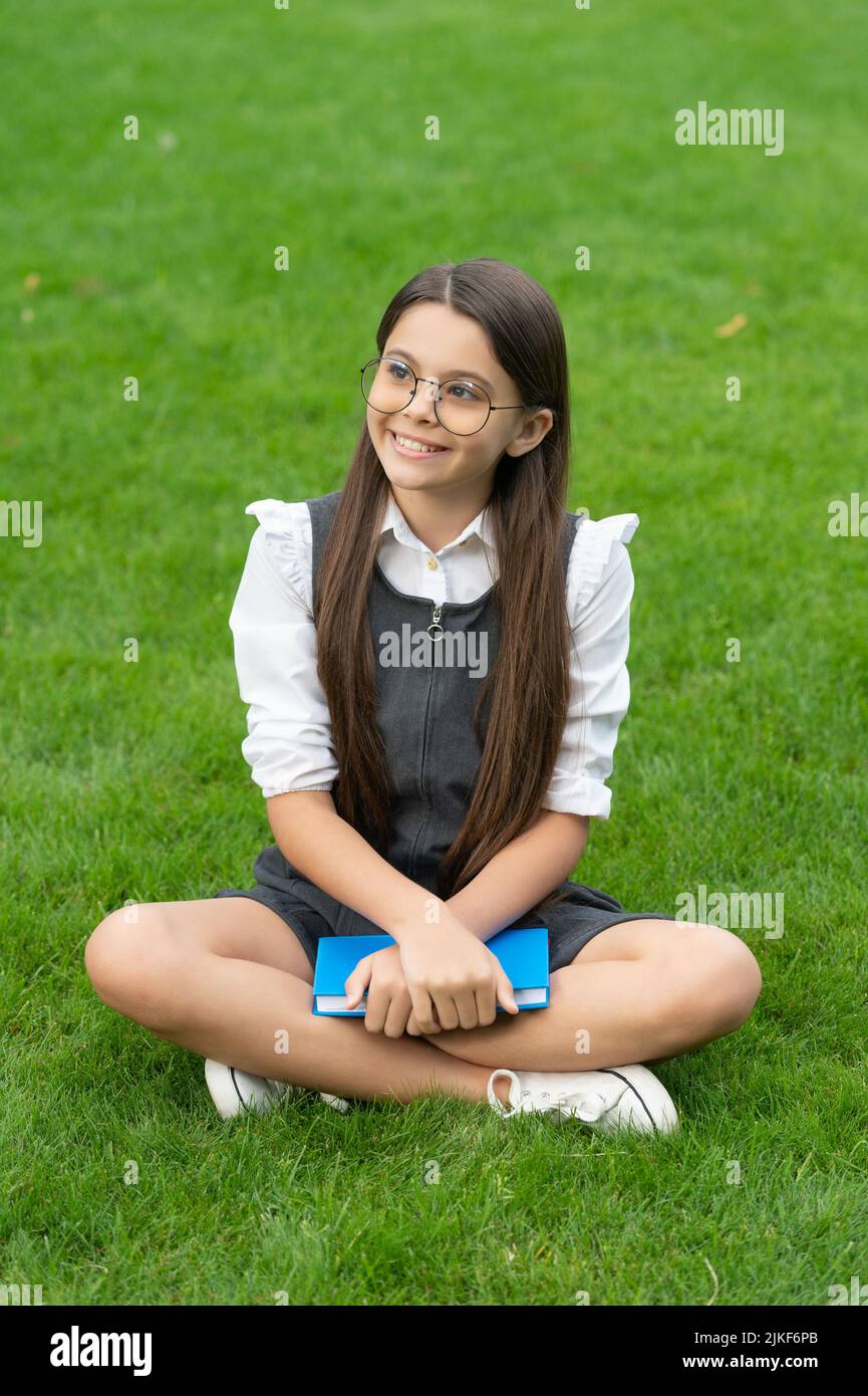 Happy teen school girl sitting legs crossed on grass. School and