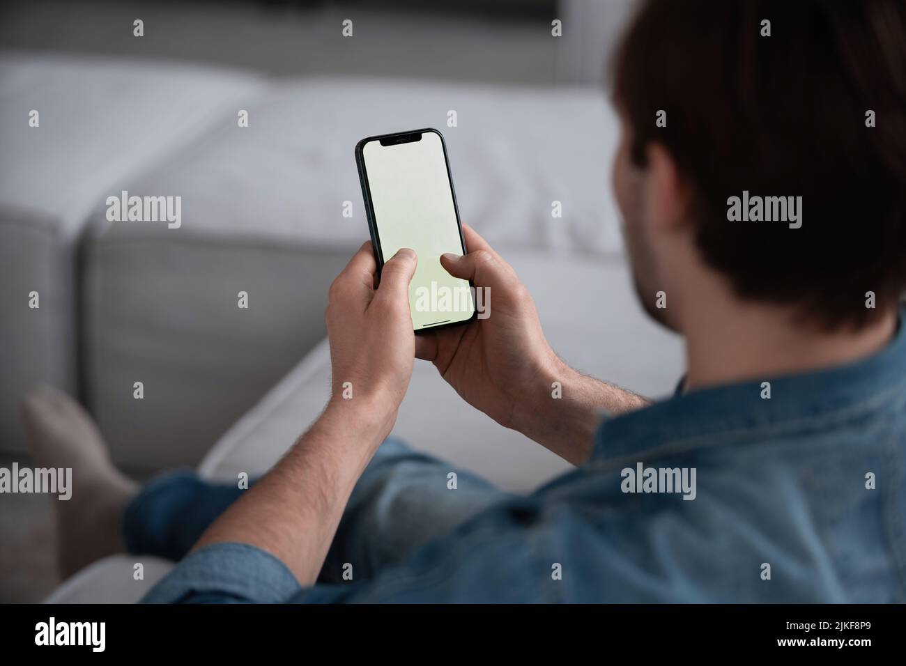 People And Technology Concept. Over The Shoulder View Of Unrecognizable Man Using Smart Phone With White Empty Screen For Mockup, Sitting At Home, Mak Stock Photo