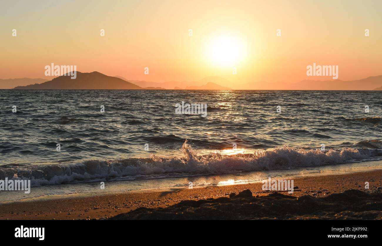 Amazing beach sunset with endless horizon and lonely figures in the distance, and incredible foamy waves. Volcanic hills in the background. Stock Photo