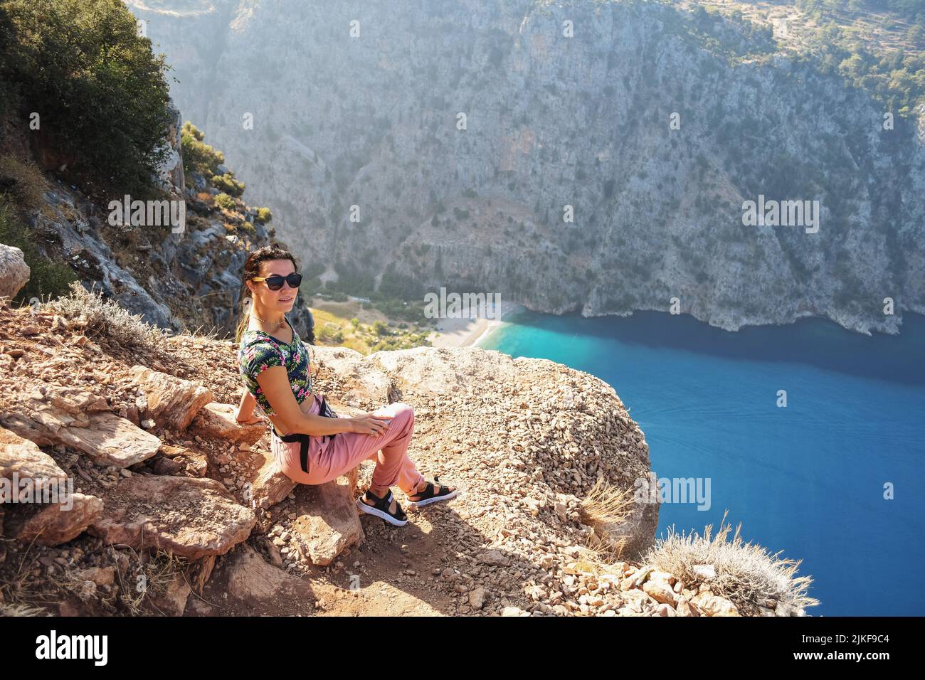 Young woman looks at the Butterfly Valley from above, sitting on the rocks. Landscape Oludeniz, Turkey. Stock Photo