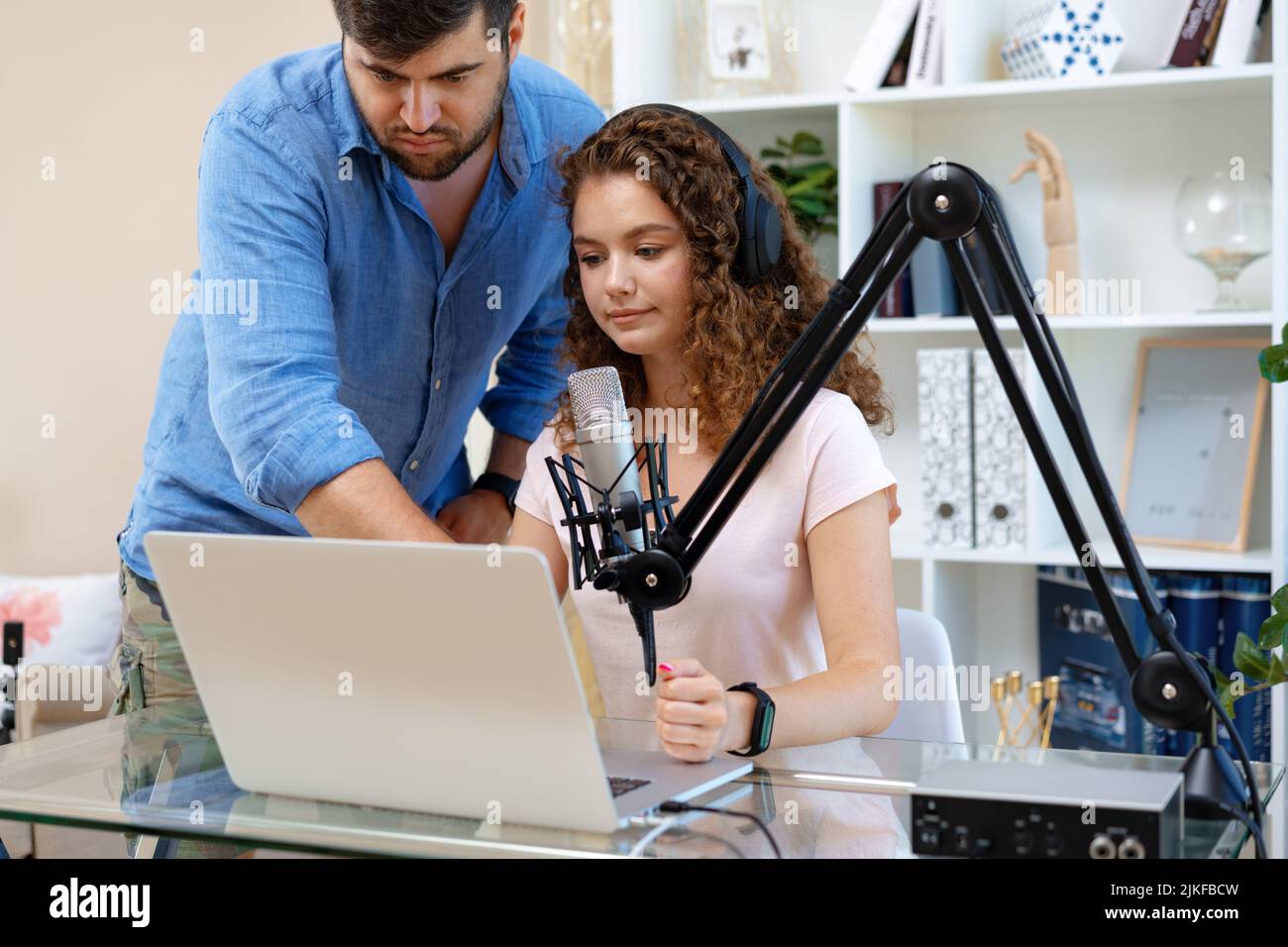 Female radio host recording podcast in studio, man colleague helps her