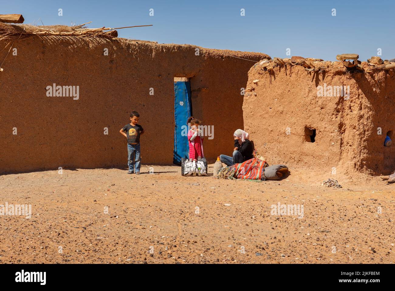 Errachidia Province, Morocco - October 15, 2015: Berber huts in the Sahara Desert. A sad Berber woman sits near the wall of the house outside, the chi Stock Photo