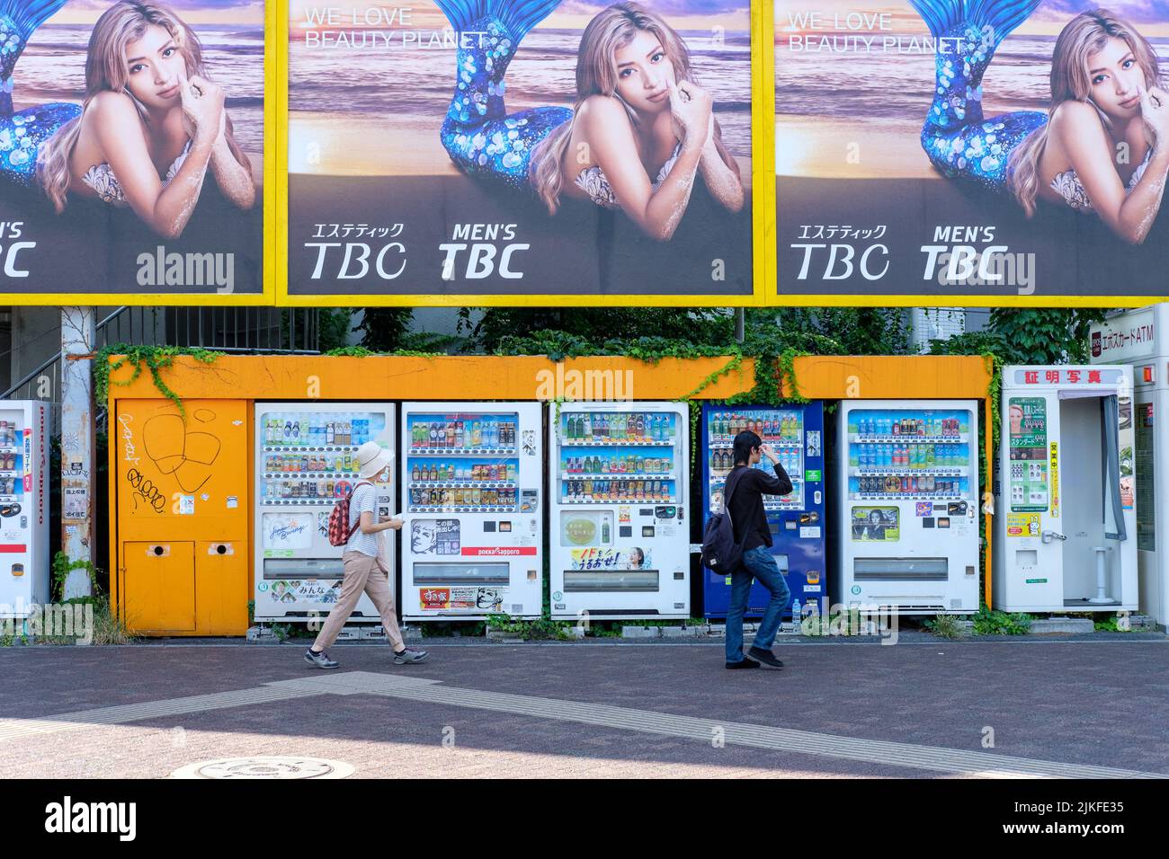 TOKYO, JAPAN - AUGUST 4, 2019: People pass by a collection of typically Japanese vending machines and billboards in Tokyo, Japan on August 4, 2019. Stock Photo