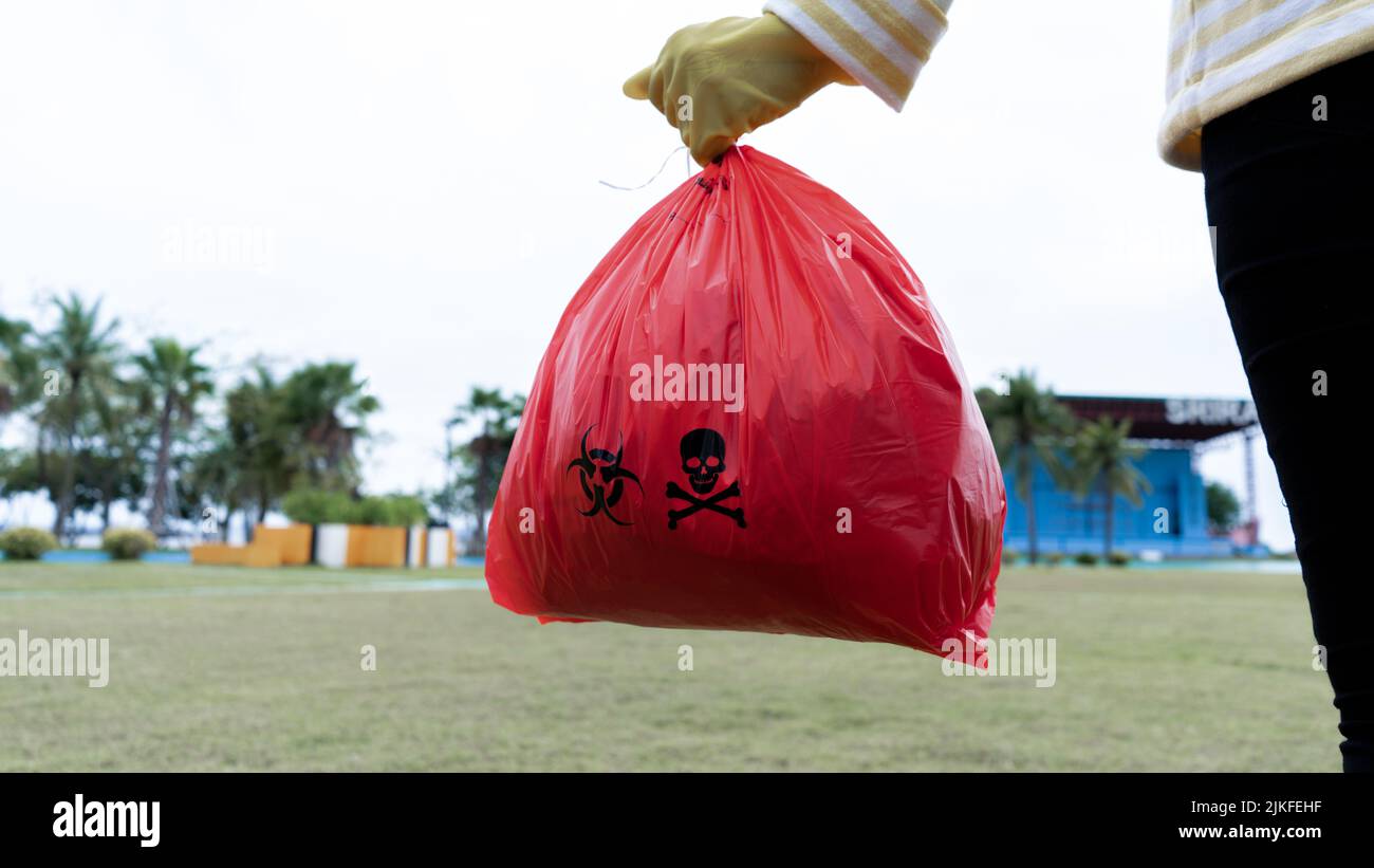 Woman holding red Bag Hazardous waste on the Park. Woman wearing yellow gloves holding red bag Stock Photo