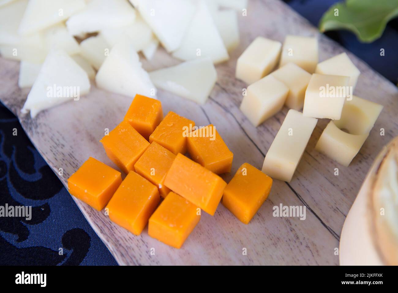 Cubes of cheese over white wooden cutting board. Closeup Stock Photo