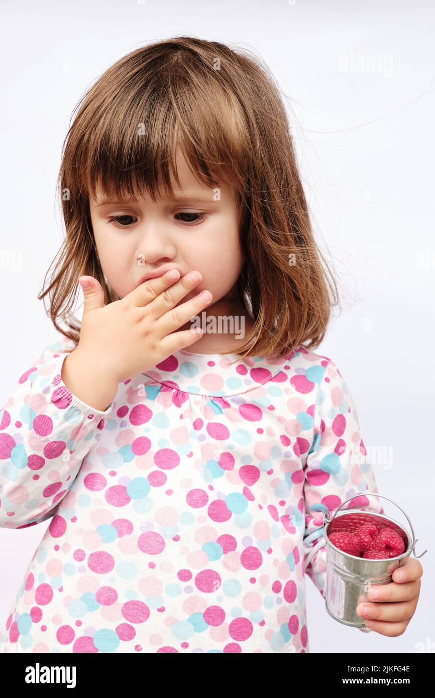 Little baby eating raspberry from decorative metal bucket. Child