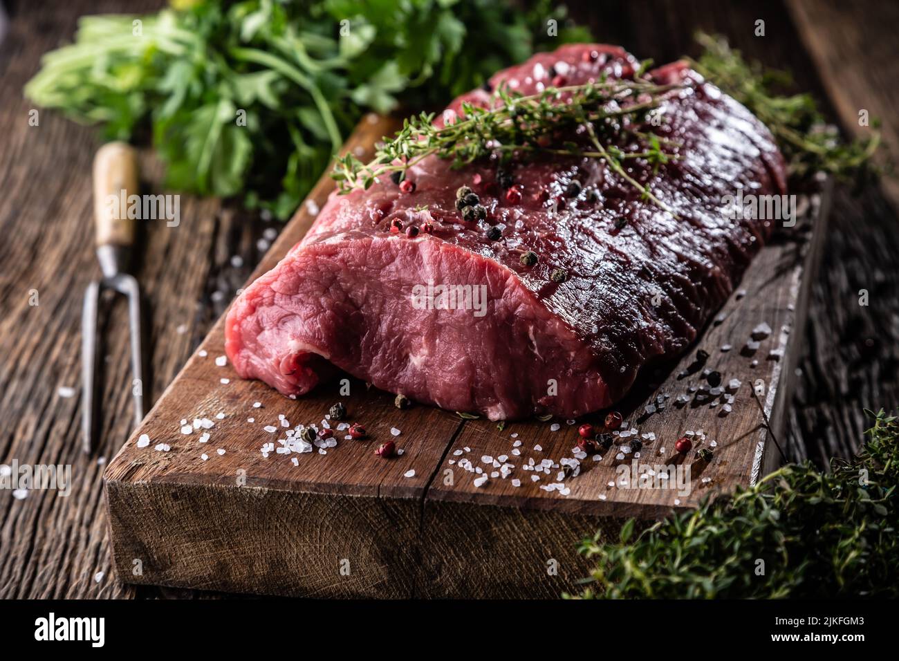 Raw rib eye steak whole on a wooden board with herbs - Close up. Stock Photo