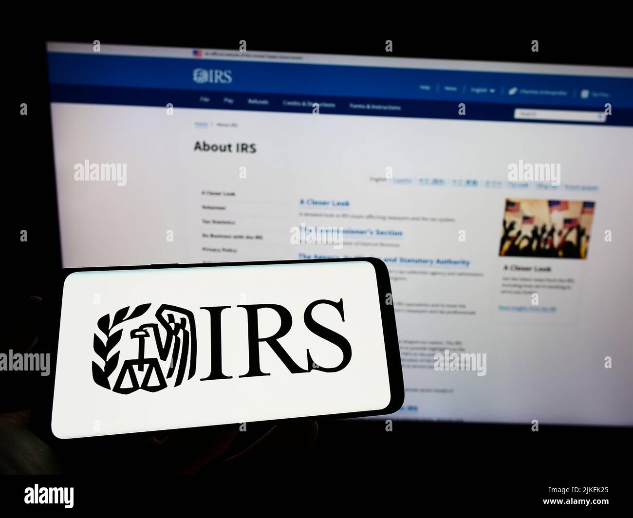 Person holding mobile phone with logo of US Internal Revenue Service (IRS) on screen in front of web page. Focus on phone display. Stock Photo