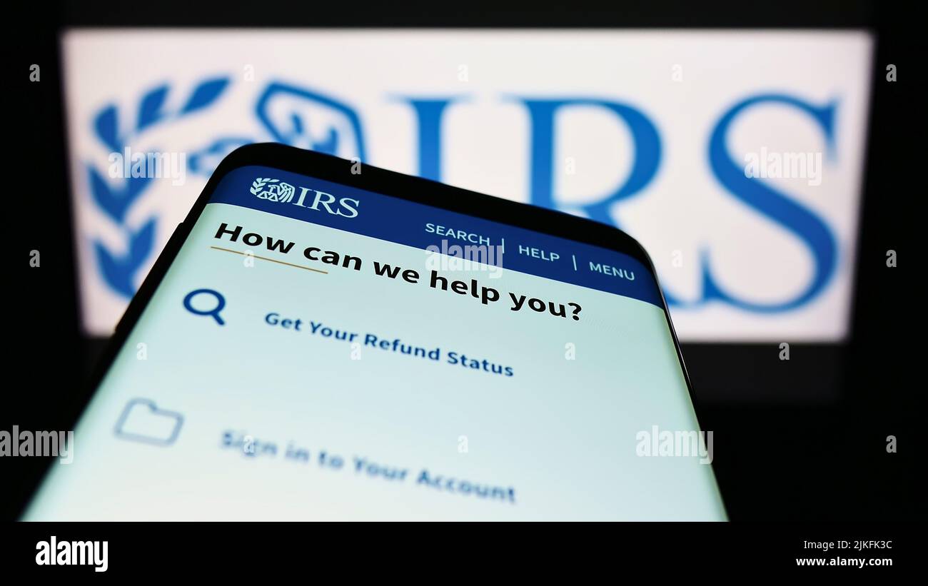 Mobile phone with website of United States Internal Revenue Service (IRS) on screen in front of logo. Focus on top-left of phone display. Stock Photo