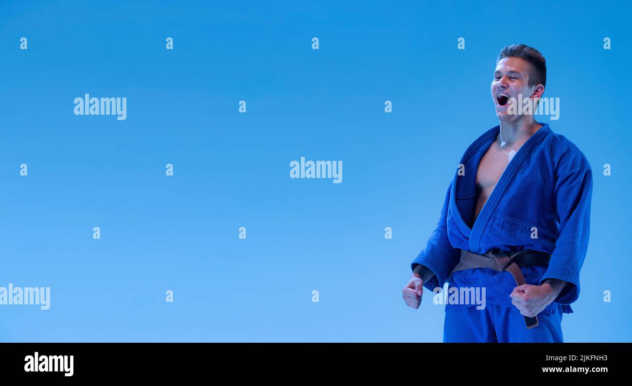 Portrait of young sportive man, martial art coach posing isolated over blue studio background in neon light Stock Photo