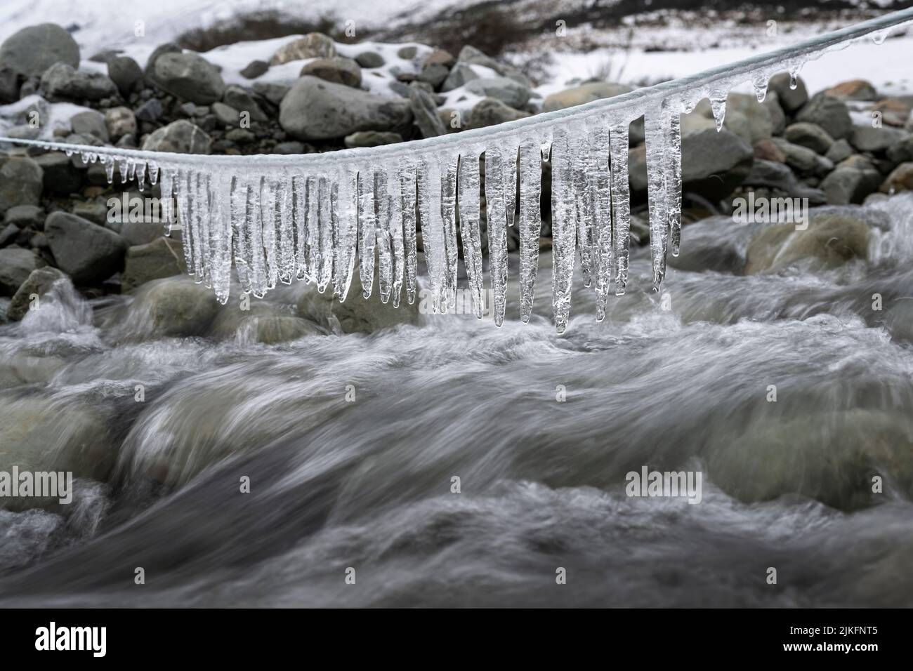 Icicle hanging above the stream with running water Stock Photo