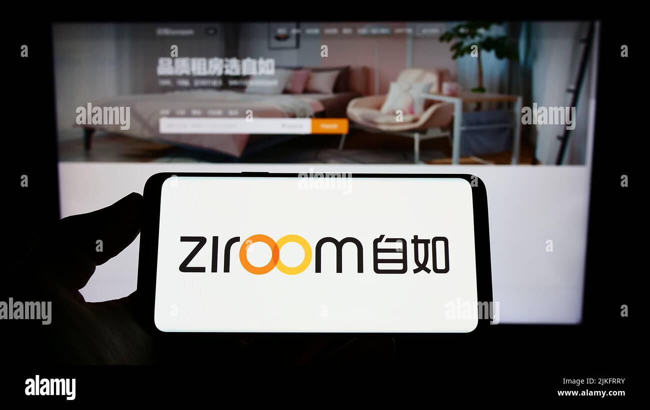 Person holding smartphone with logo of Chinese real estate company Ziroom on screen in front of website. Focus on phone display. Stock Photo