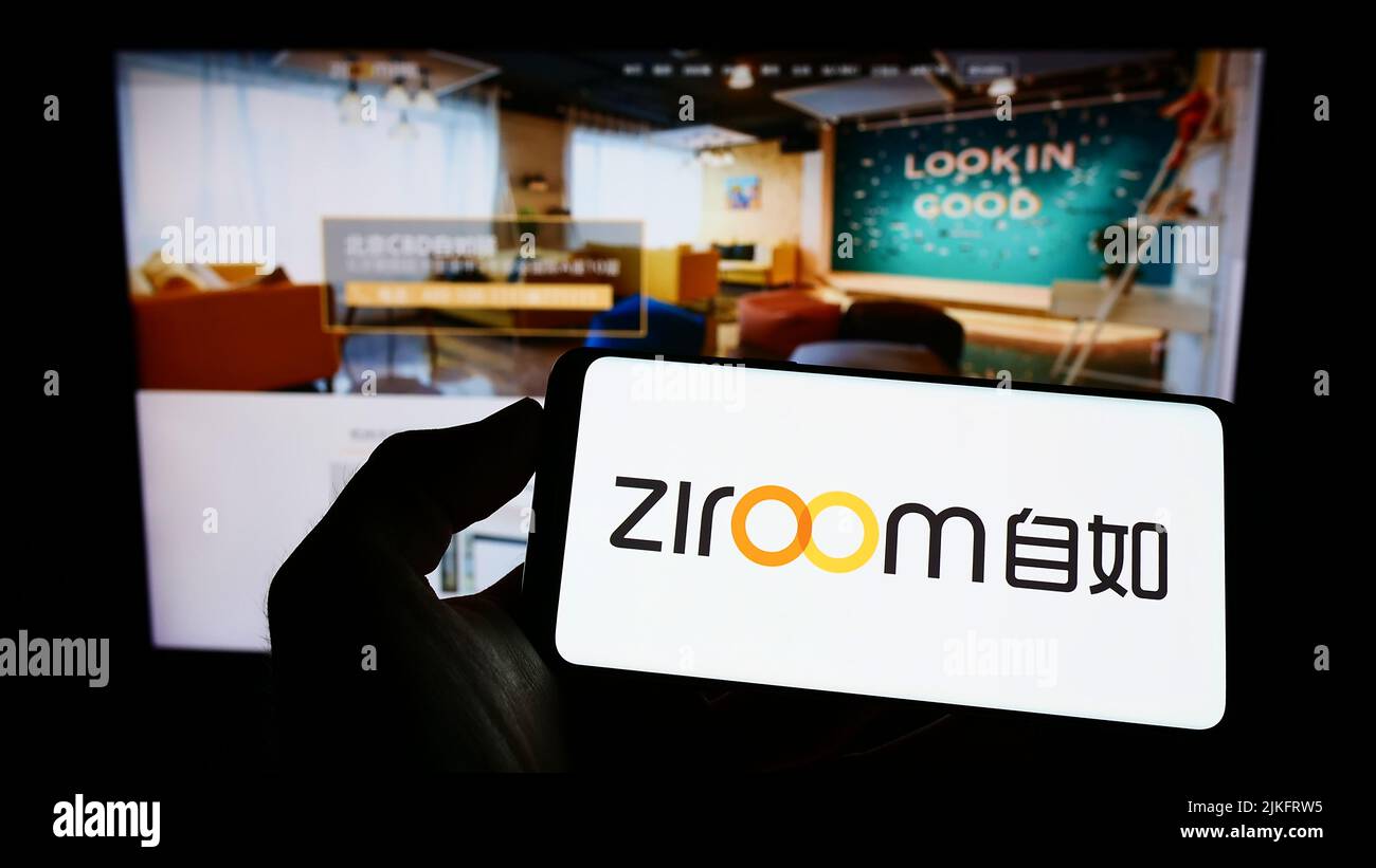 Person holding mobile phone with logo of Chinese real estate company Ziroom on screen in front of business web page. Focus on phone display. Stock Photo