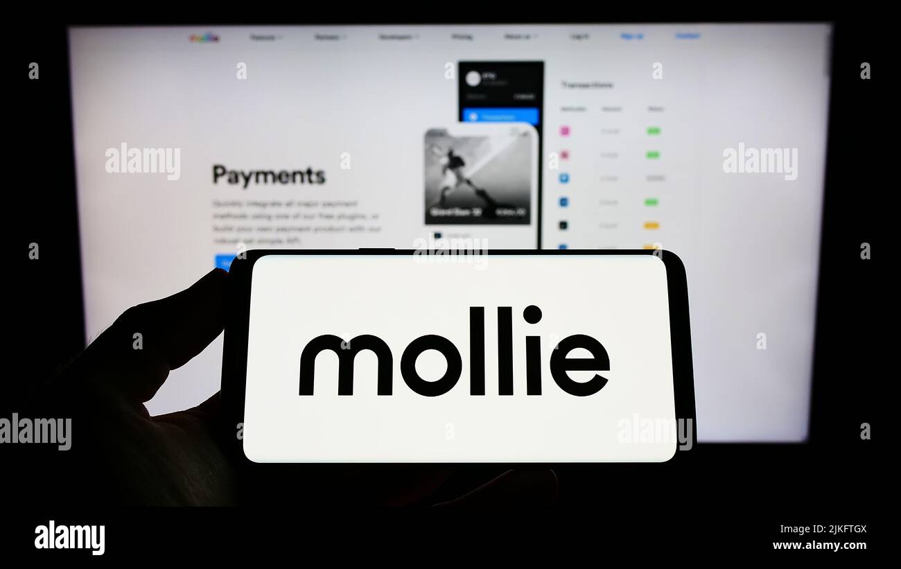 Person holding smartphone with logo of Dutch payments company Mollie B.V. on screen in front of website. Focus on phone display. Stock Photo
