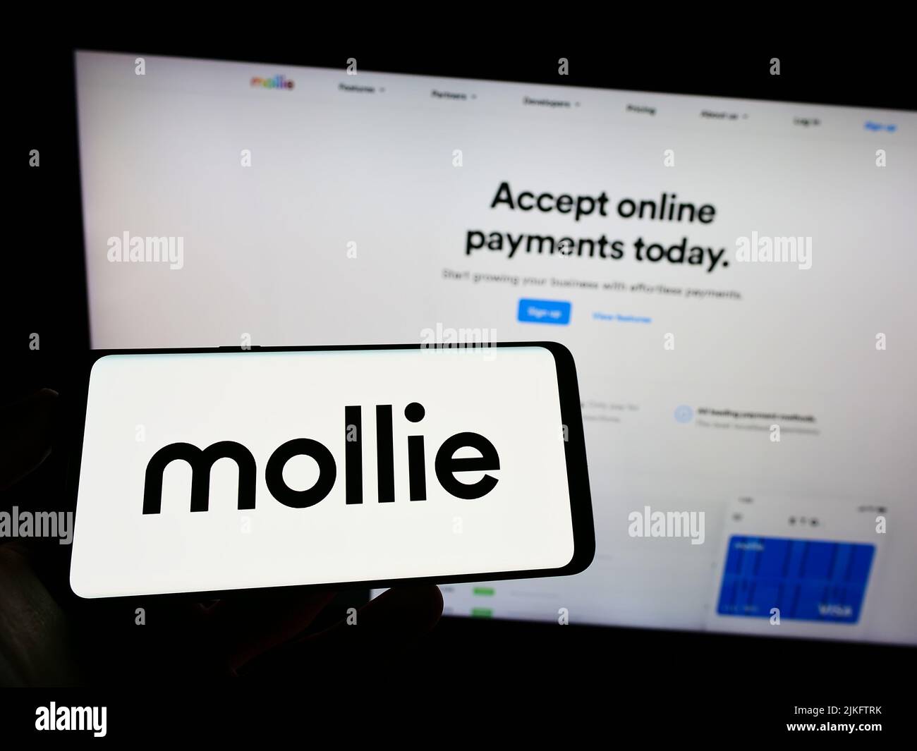 Person holding cellphone with logo of Dutch payments company Mollie B.V. on screen in front of business webpage. Focus on phone display. Stock Photo