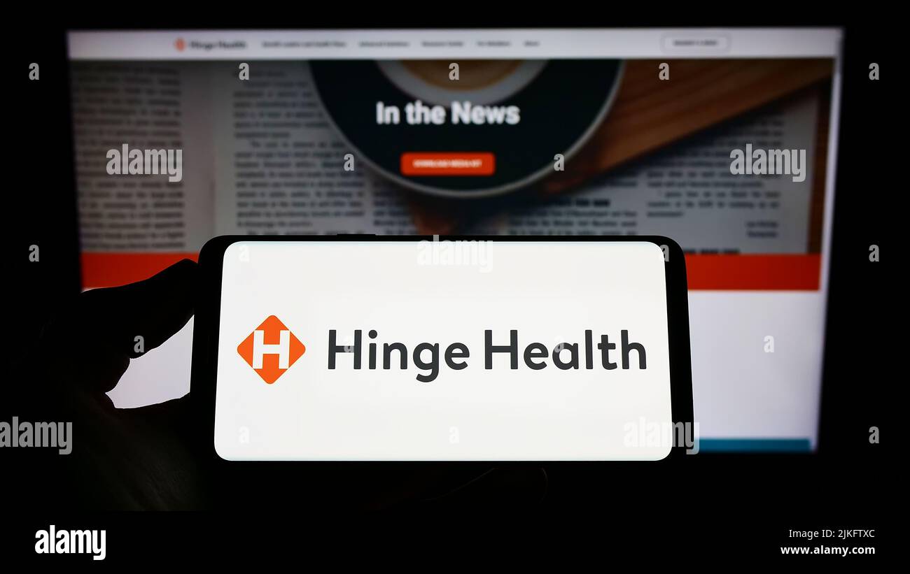 Person holding smartphone with logo of US digital clinic company Hinge Health Inc. on screen in front of website. Focus on phone display. Stock Photo