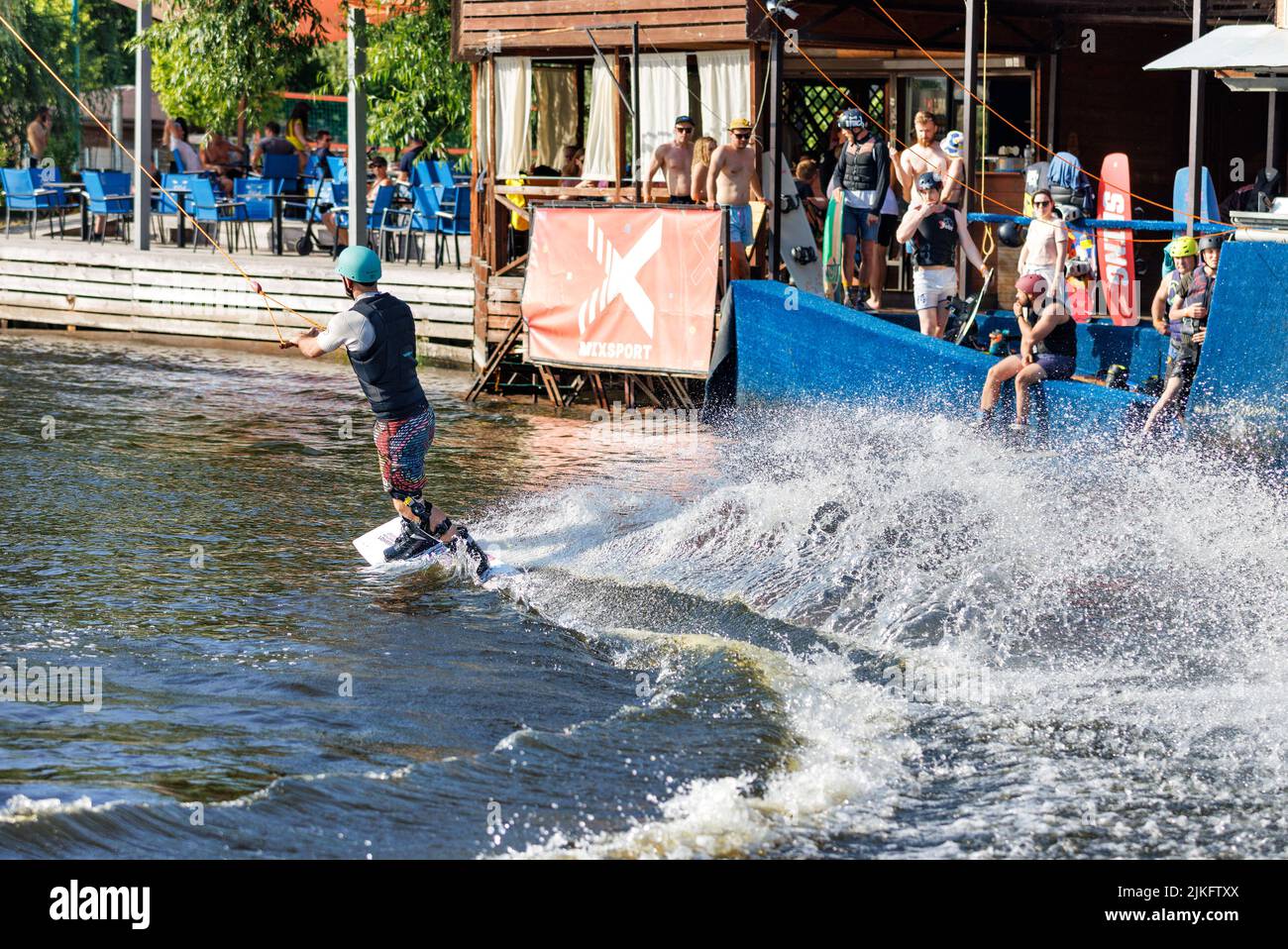 An athlete wakeboarder dynamically makes a U-turn on a water board in front of the stands of spectators on a summer day. 06.19.1922. Kyiv. Ukraine. Stock Photo