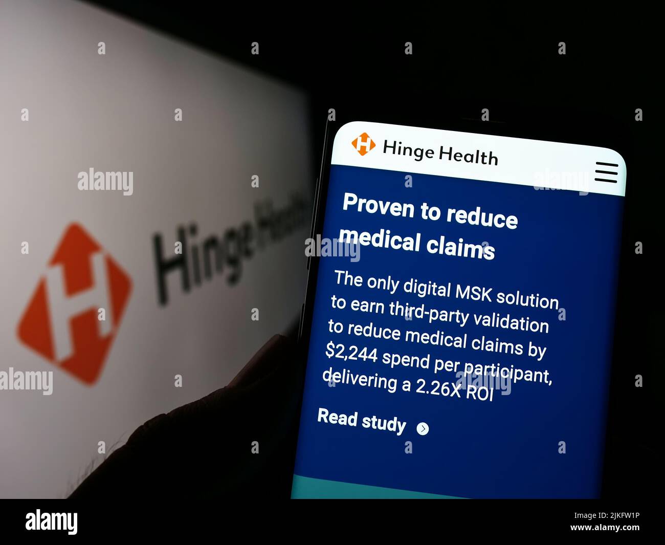 Person holding cellphone with webpage of US digital clinic company Hinge Health Inc. on screen in front of logo. Focus on center of phone display. Stock Photo