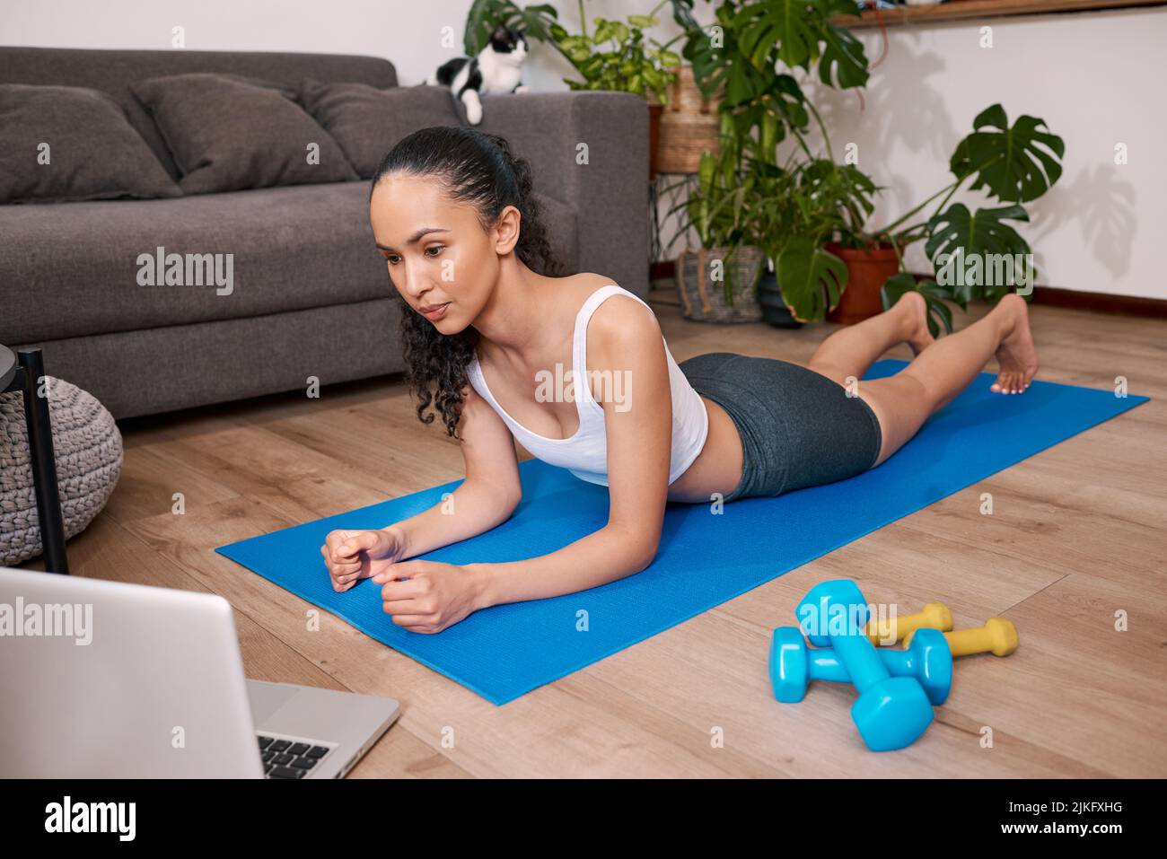 A young multi-ethnic woman checks her exercise position on laptop at ...