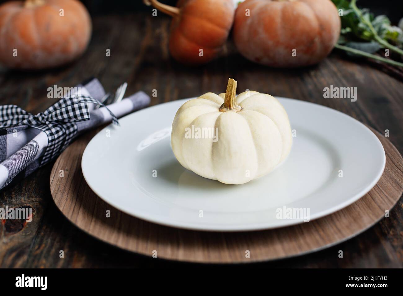 Holiday place setting with plate, napkin, and silverware on a Thanksgiving Day decorated table. White and Orange pumpkins. Selective focus with blurre Stock Photo