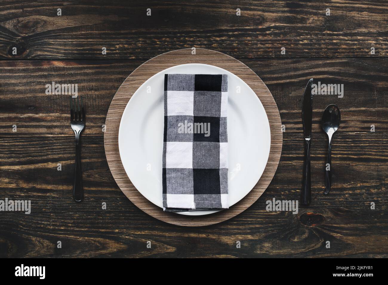 Vintage flat lay of a place setting with buffalo plaid napkin, silverware and charger over a rustic wood table. Top view. Stock Photo