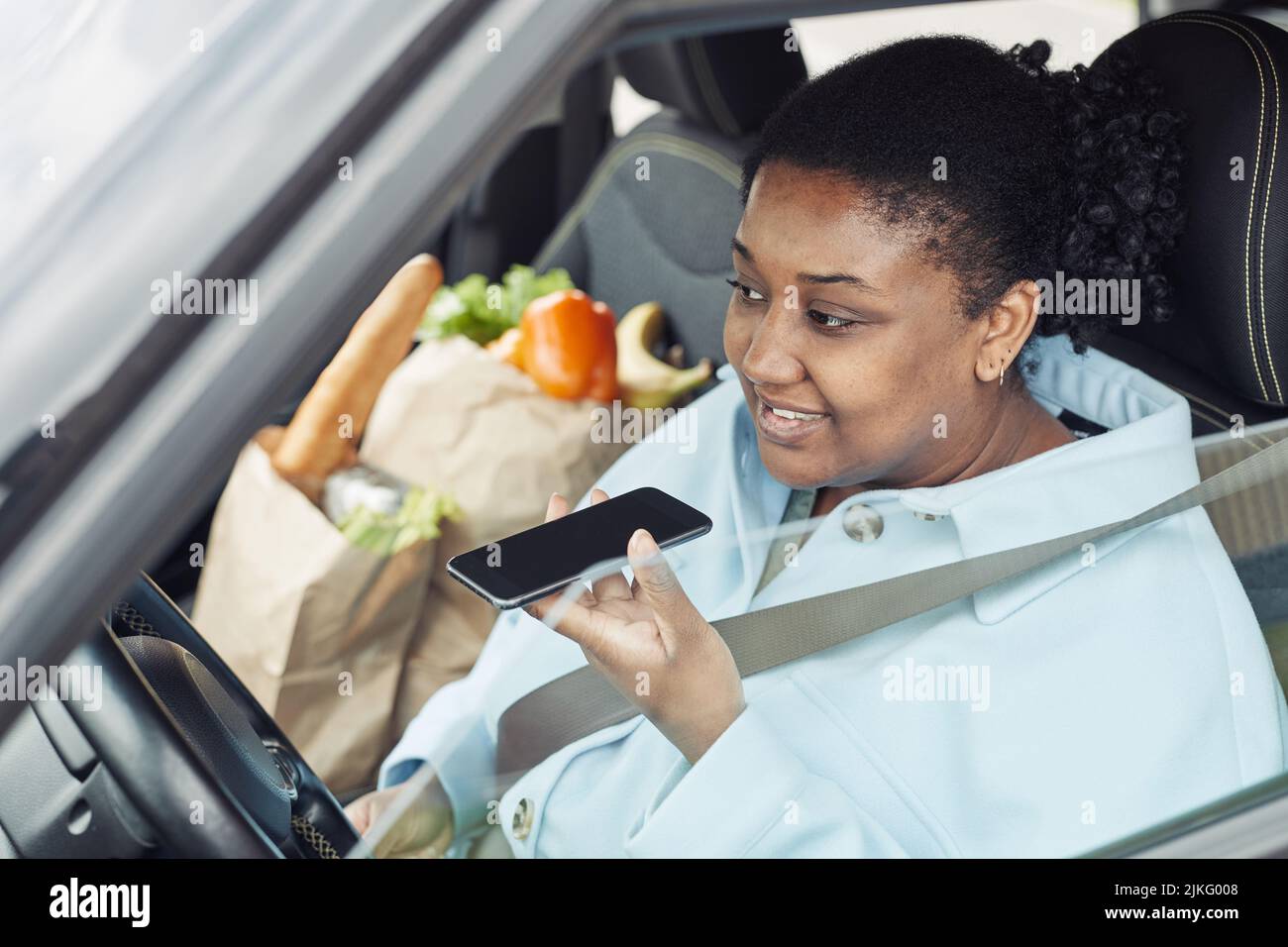 Portrait of young black woman recording voice message while sitting in car with seatbelt on Stock Photo