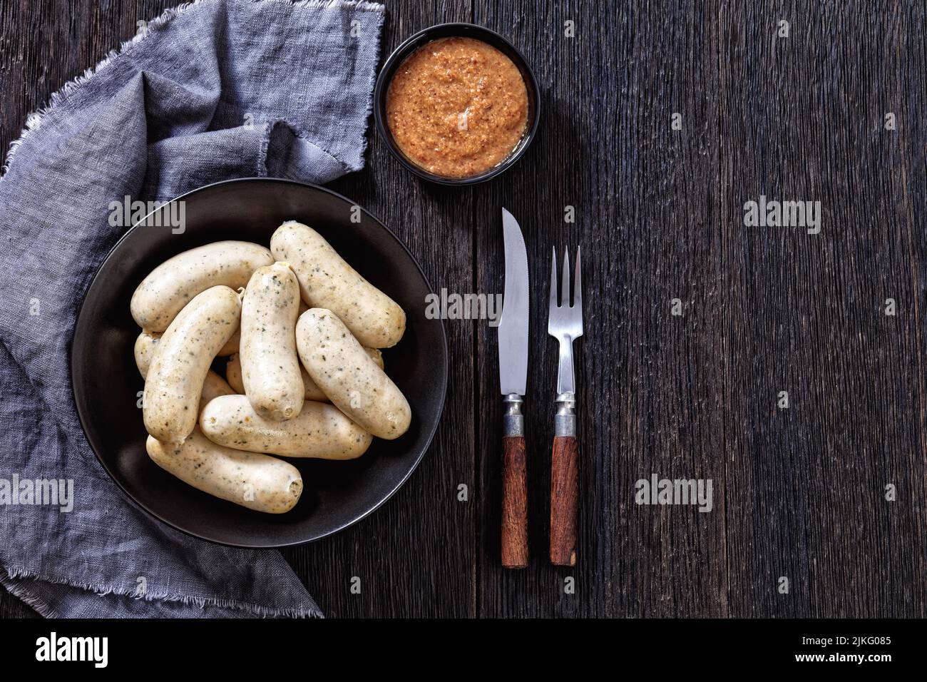 Weisswurst in black bowl, white sausages of minced veal, pork back bacon, spices and parsley, served with sweet mustard, flat lay, free space Stock Photo