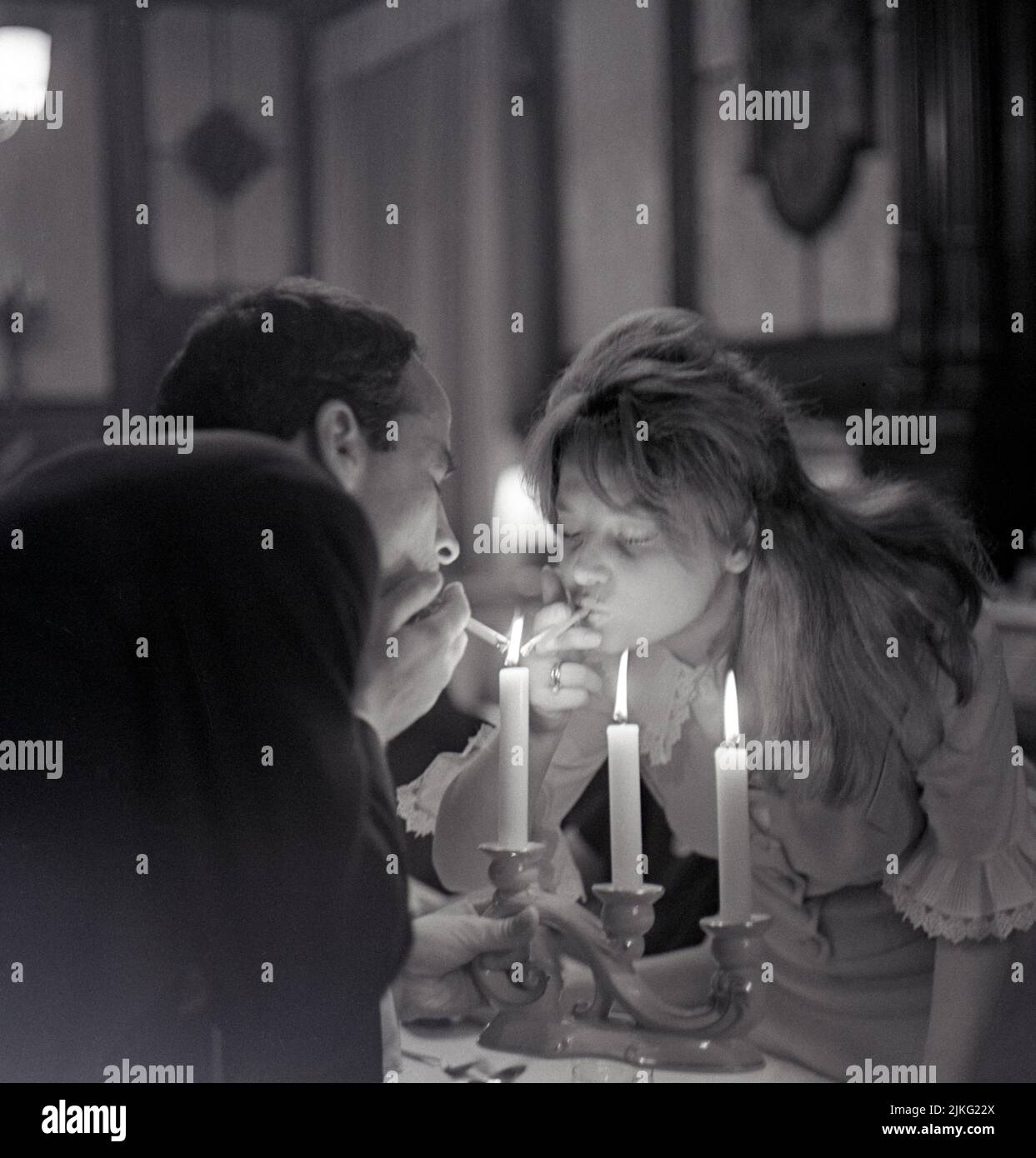 01.09.1964, German Democratic Republic, , Berlin - Young couple lighting their cigarettes at the same time on a candle. 00S640901D001CAROEX.JPG [MODEL Stock Photo