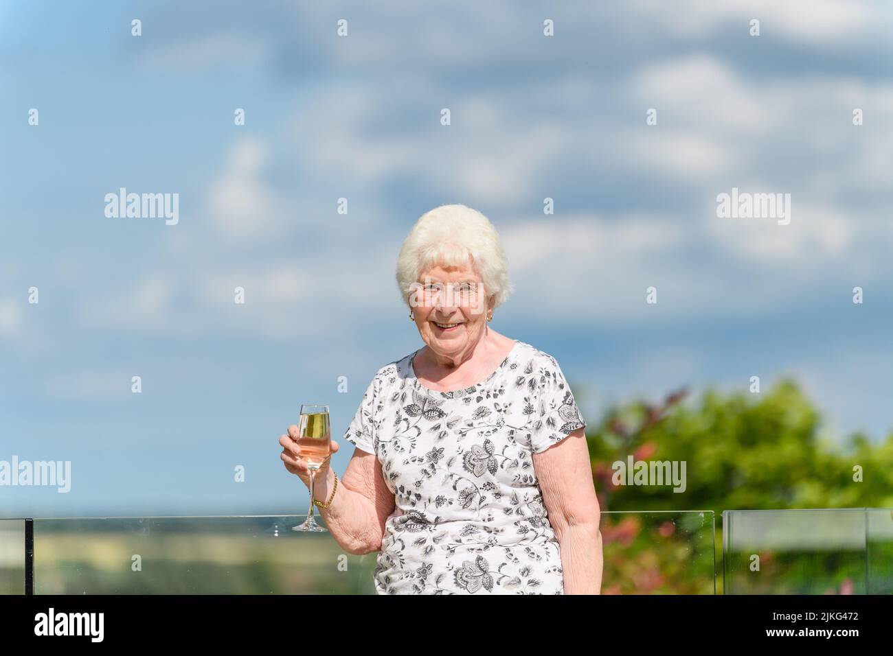A happy old Caucasian woman posing with a glass of white wine Stock Photo