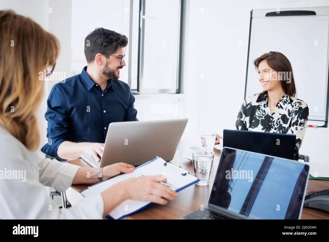 Businesswomen and businessman sitting at desk and using laptop while having a meeting in a conference room. Stock Photo